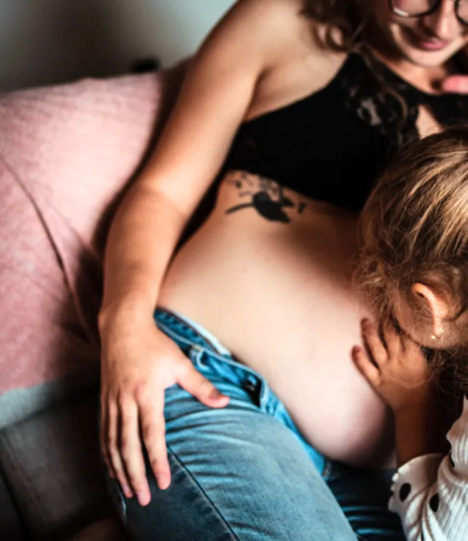 Image of a young girl, kissing her mother's pregnant belly. Image represents the top of page for MSP Doula, an inclusive and informed doula support service in the Twin Cities of Minneapolis and Saint Paul, Minnesota.