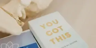 A light blue affirmation card with gold letters reading YOU GOT THIS lies on a surface next to another item, with part of a decorative object visible in the background—perfect for birth plan coaching support.