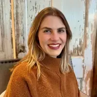 Headshot of Meredith Kramer for Jillian Carpenter Birth Doula Testimonial. A woman with straight, shoulder-length blonde hair and a brown sweater smiles while sitting indoors in front of rustic wooden panels.
