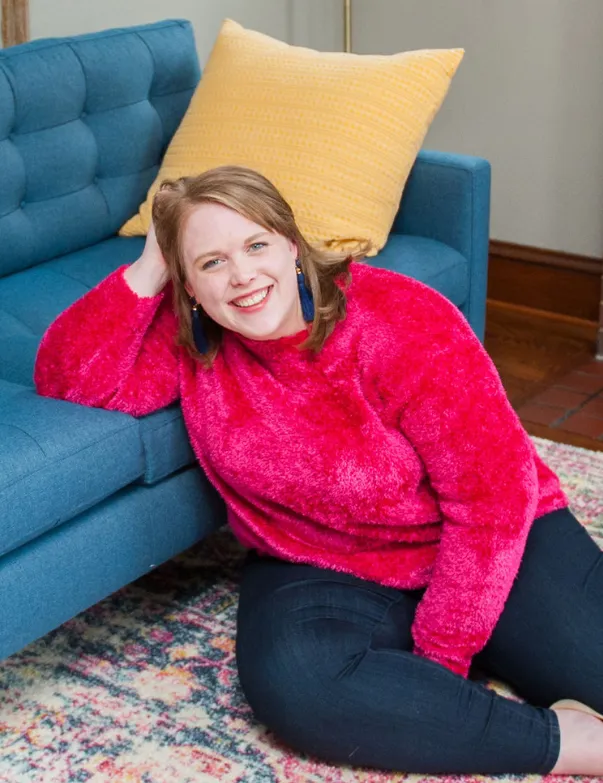 An image of Twin Cities doula, Jillian Carpenter, smiling at the camera while lounging on her blue couch in her Minneapolis, Minnesota home.