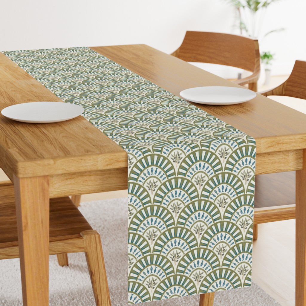 Small-scale geometric fan and leaf print in muted teal, olive, cream, and beige used as a table runner in a warm wood dining room setting.