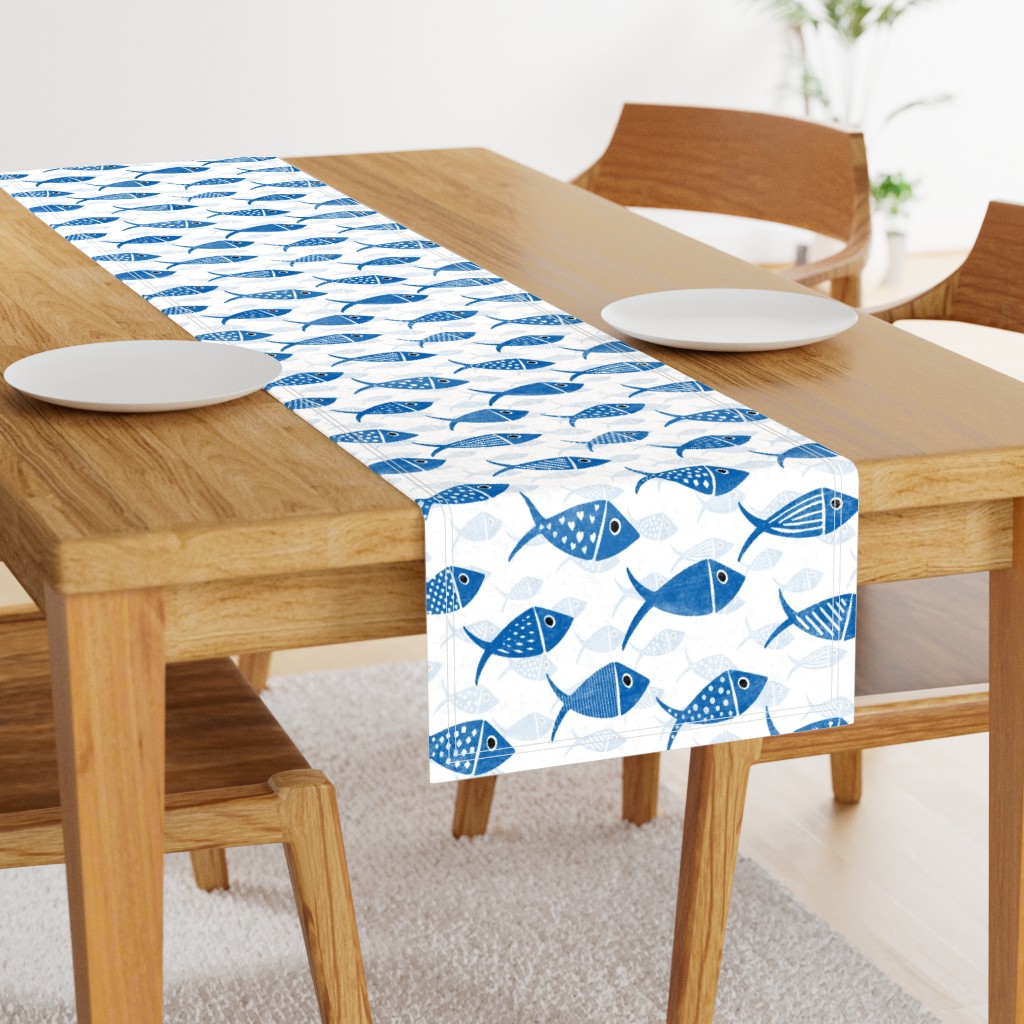 Blue and white Nautical School of Fish shown on a table runner across a wooden dining table with white place settings.