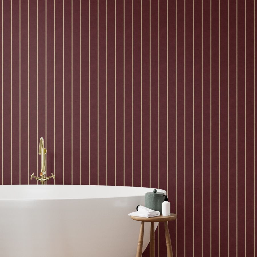 Deep burgundy wallpaper with narrow cream vertical stripes behind a bathtub with a brass tap.
