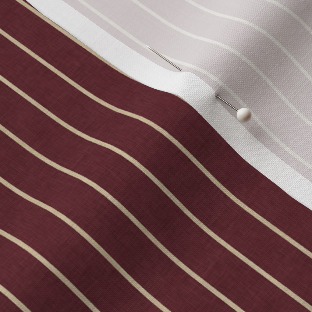 Close-up of overlapping striped fabric in burgundy and pale greige colourways, with cream and white lines and a small pin.