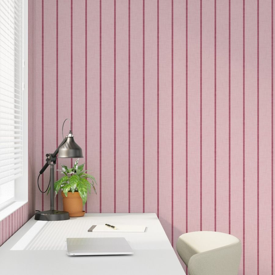 Soft pink Roselk Design wallpaper with narrow burgundy stripes behind a desk, lamp and small stool in a home office setting.