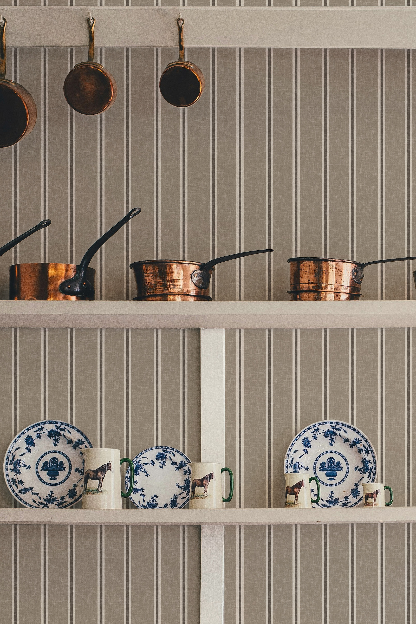 Dark beige Nantucket Linen Textured Stripe wallpaper in a kitchen setting with copper pans, open shelving and decorative plates.