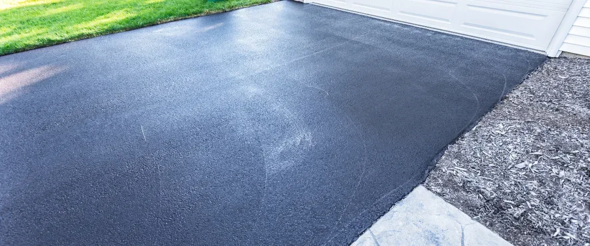 Newly sealed black asphalt driveway in front of garage
