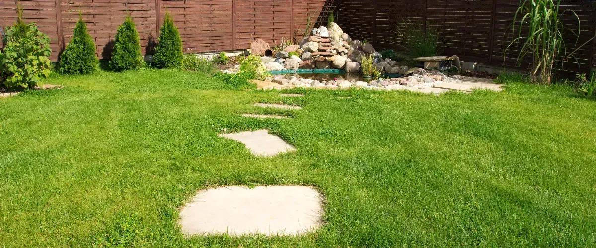 Backyard with stepping stones leading to a small pond and rock feature