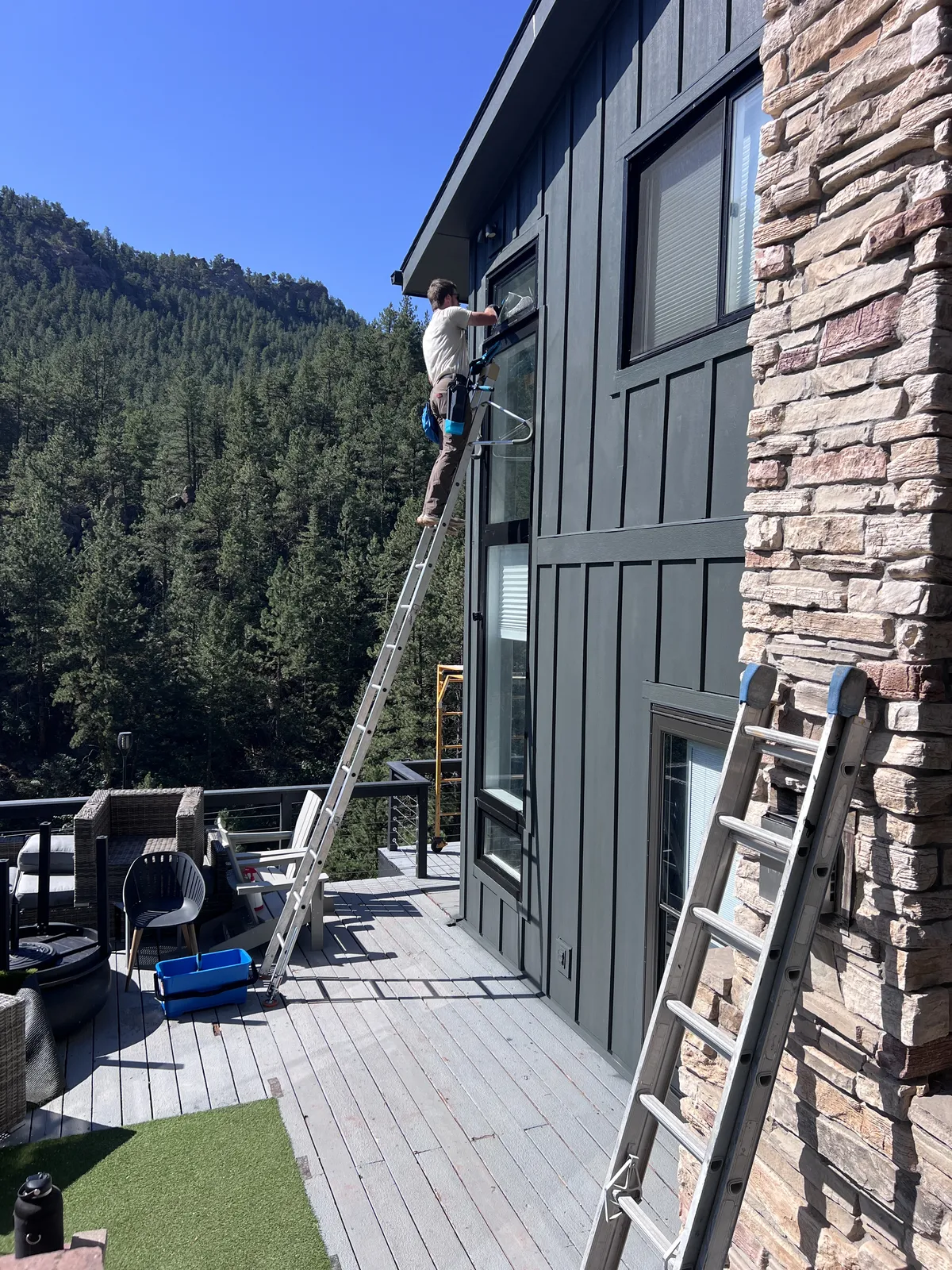 Technician on a ladder cleaning exterior windows of a Colorado mountain cabin