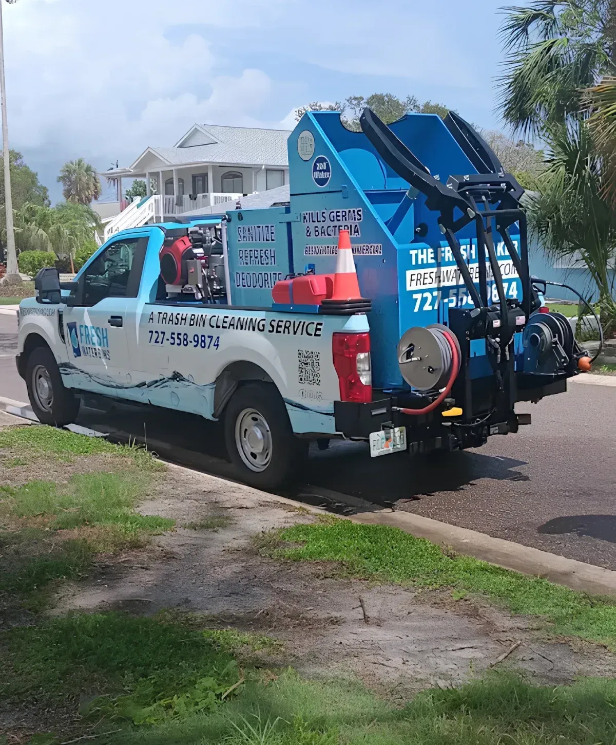 A light blue and white Fresh Water Bins truck parked on a residential street with a trash bin cleaning sign.