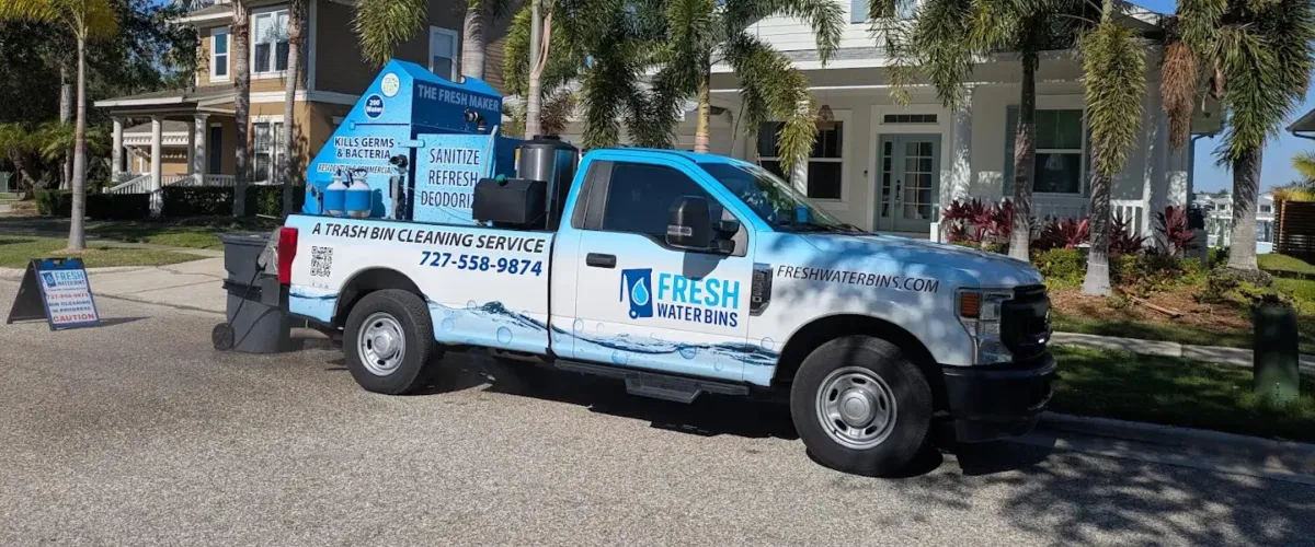 A white and blue Fresh Waters bin cleaning service truck with cleaning equipment in the back, parked on a street.