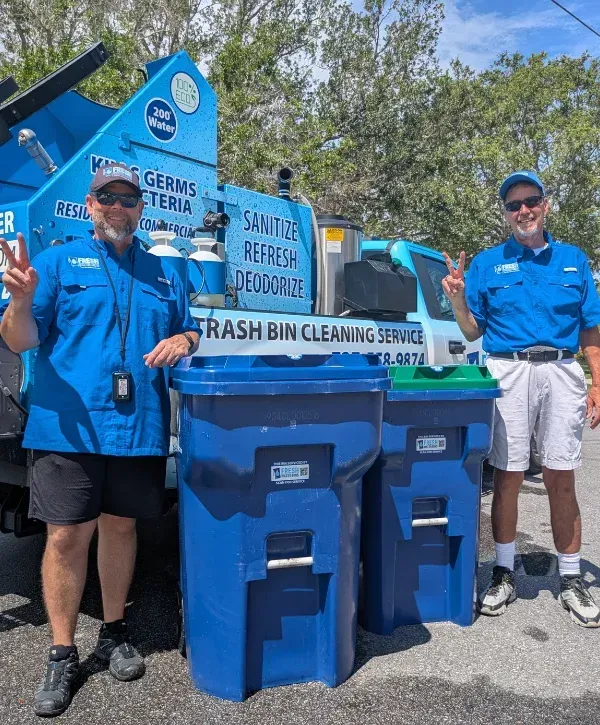 Two men in blue shirts and sunglasses giving peace signs beside a 'Trash Bin Cleaning Service' truck and blue bins.
