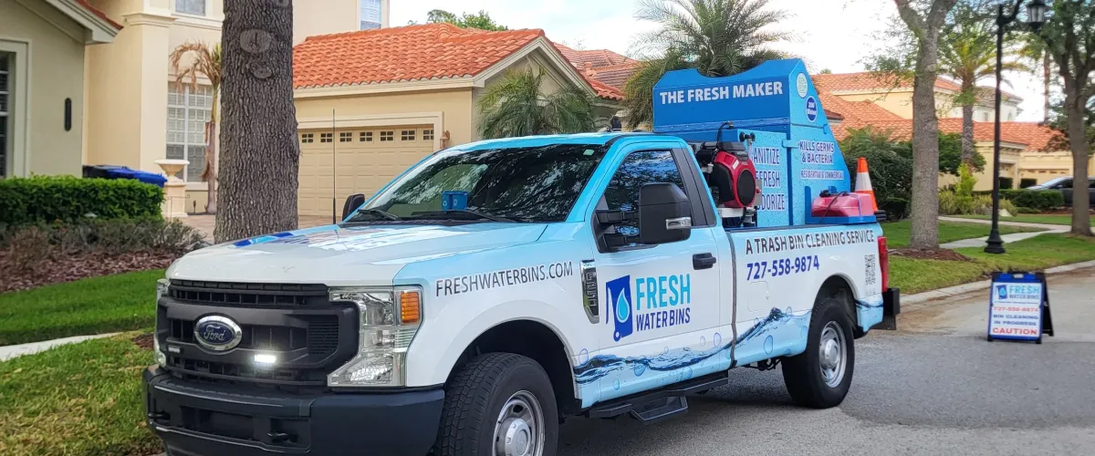 A white and blue Fresh Water Bins trash bin cleaning service truck parked on a residential street in front of houses.