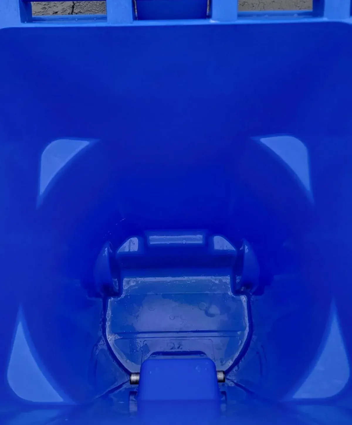 A top-down view looking into the deep blue interior of an empty, slightly textured recycling bin.