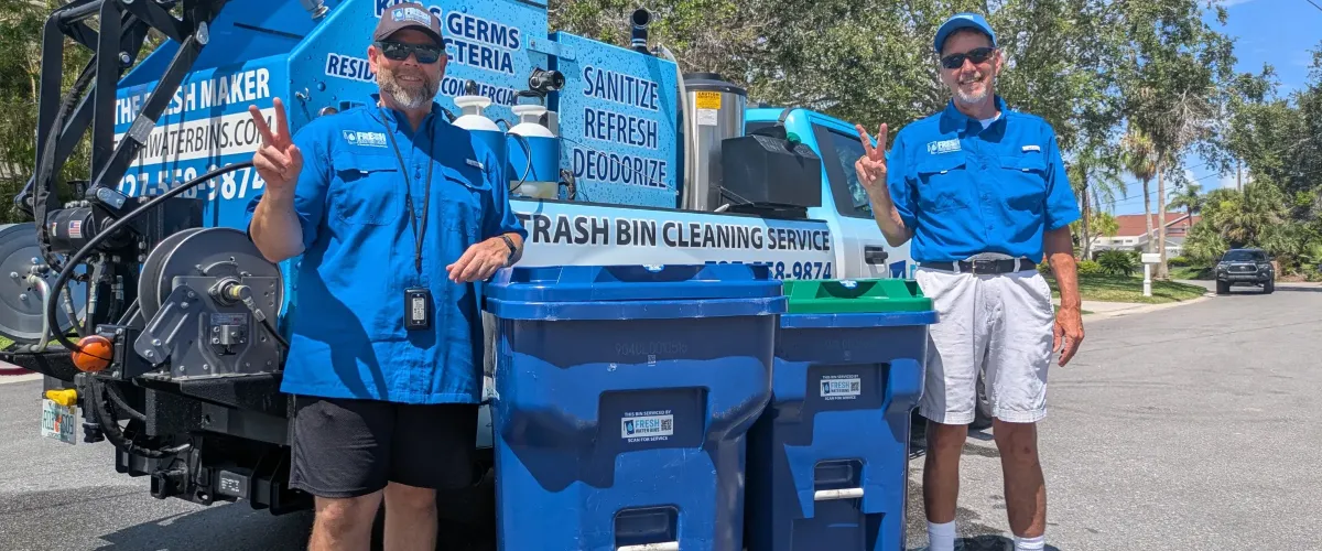 Two men in blue uniforms and sunglasses give peace signs in front of a Fresh Water Bins cleaning truck and two bins.