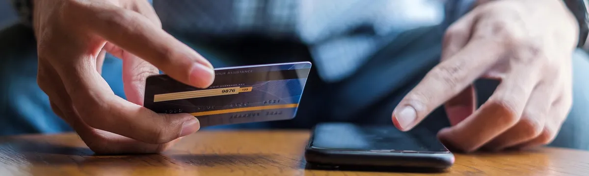 Man looking at phone holding credit card