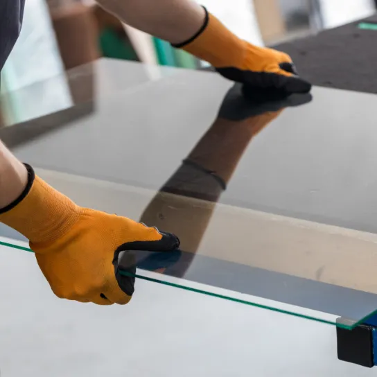 A person wearing a yellow glove holds a glass table, showcasing their work in glass craftsmanship.