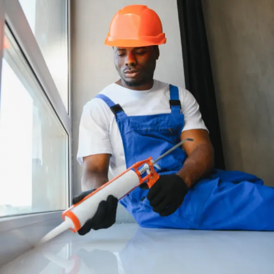 A man wearing overalls and a hard hat holds a drill, ready for construction work.