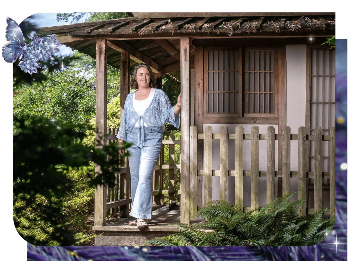 Chelsea Fournier, founder of Well Built Business, wearing jeans, a white shirt and a blue lace shawl, standing on the porch of a Japanese tea house outside