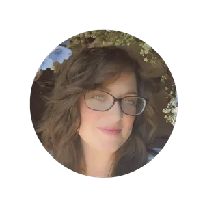 A close up headshot of Chelsey Yeager, wearing glasses and standing in front of atree