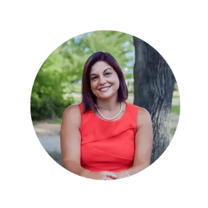Headshot of Lorraine Connell, founder of Peers Not Fears wearing a coral colored tank dress, sitting tside in front of a treeu