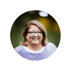 Headshot of Candice Erickson-Perham, wearing glasses and a pink and blue patterned shirt, standing in nature