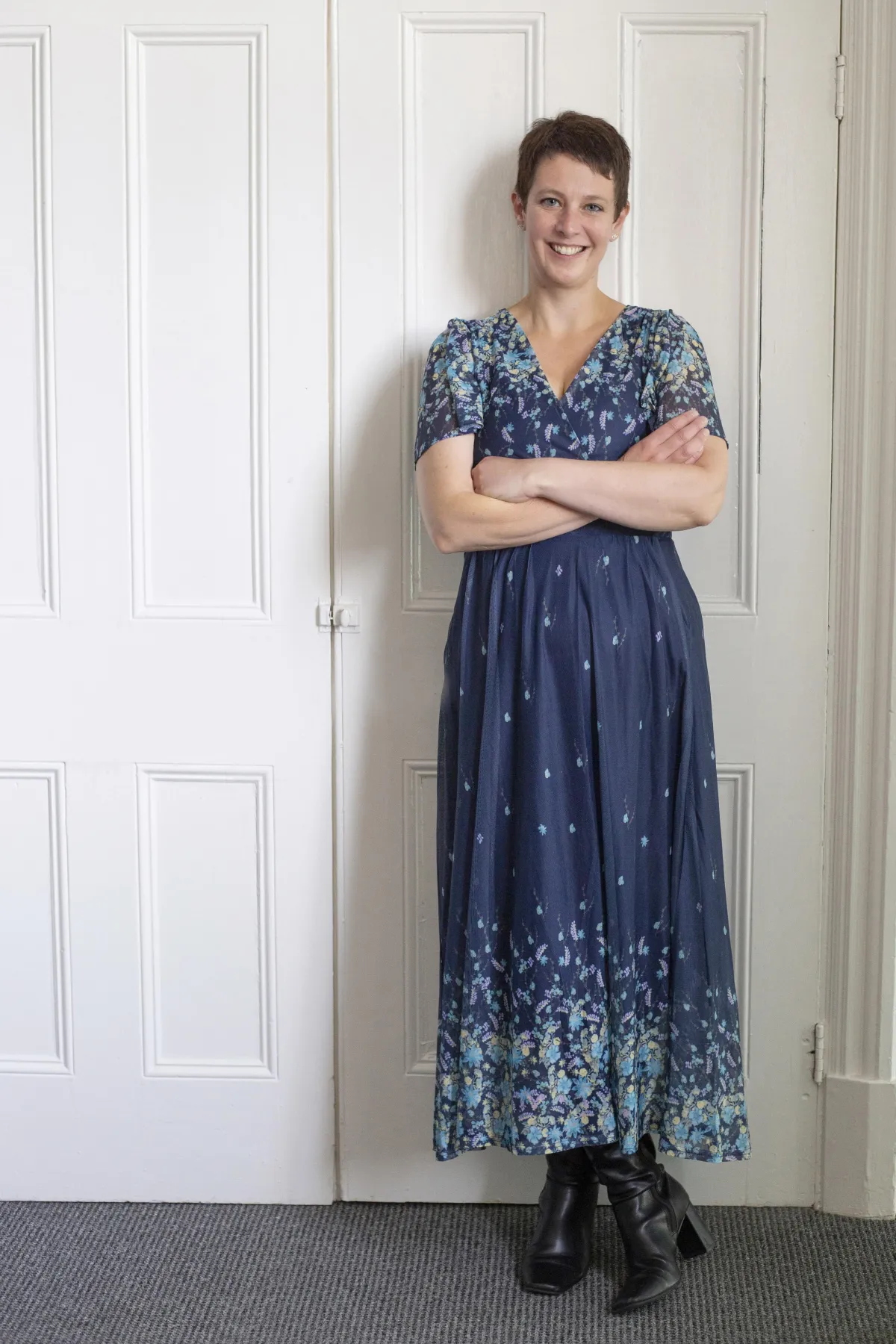 Picture of Charlotte wearing a blue dress, leaning against a white door with arms folded.