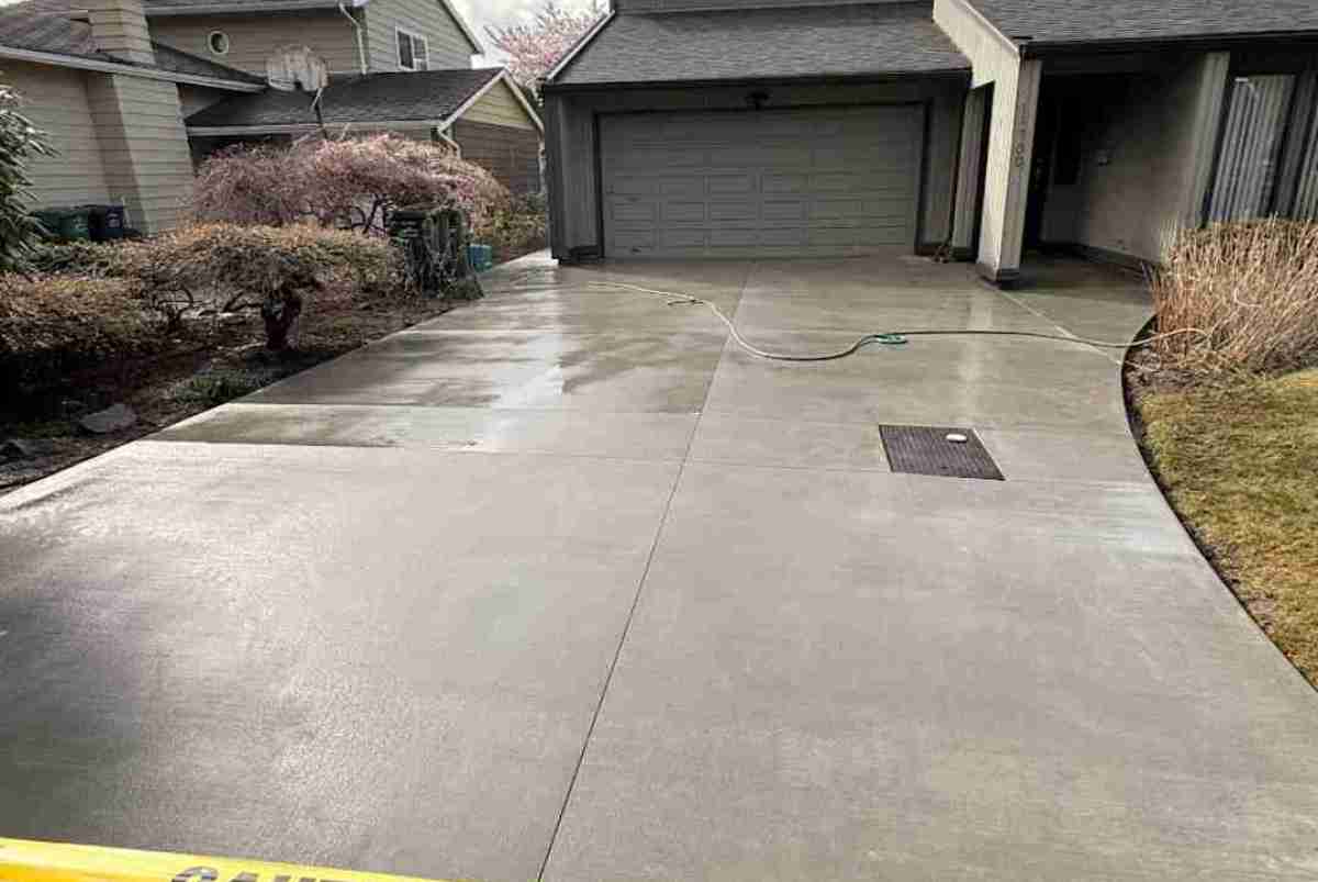A wide, modern concrete driveway with a smooth finish, leading to a contemporary home. The driveway features subtle geometric scoring and is framed by minimalist landscaping, highlighting the clean lines and craftsmanship.