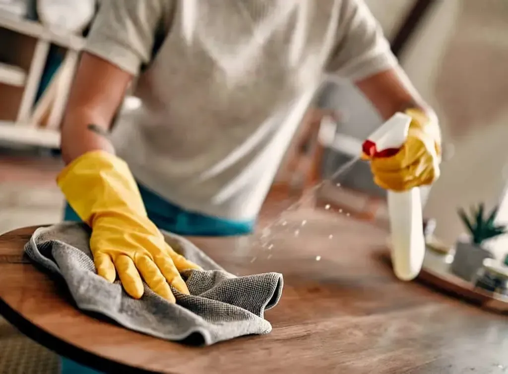 A festive arrangement of eco-friendly cleaning products with a red ribbon, surrounded by sparkling ornaments and a calendar showing today's date, set on a white marble countertop in a sunlit kitchen.