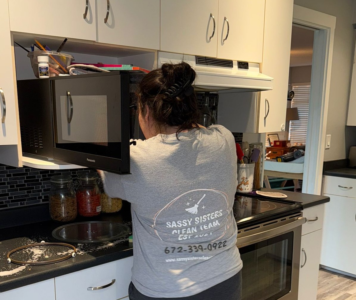A professional cleaner in branded attire smiling while dusting a modern living room, sunlight streaming through large windows, eco-friendly cleaning supplies visible on a nearby table. The scene is bright, inviting, and emphasizes cleanliness and comfort.