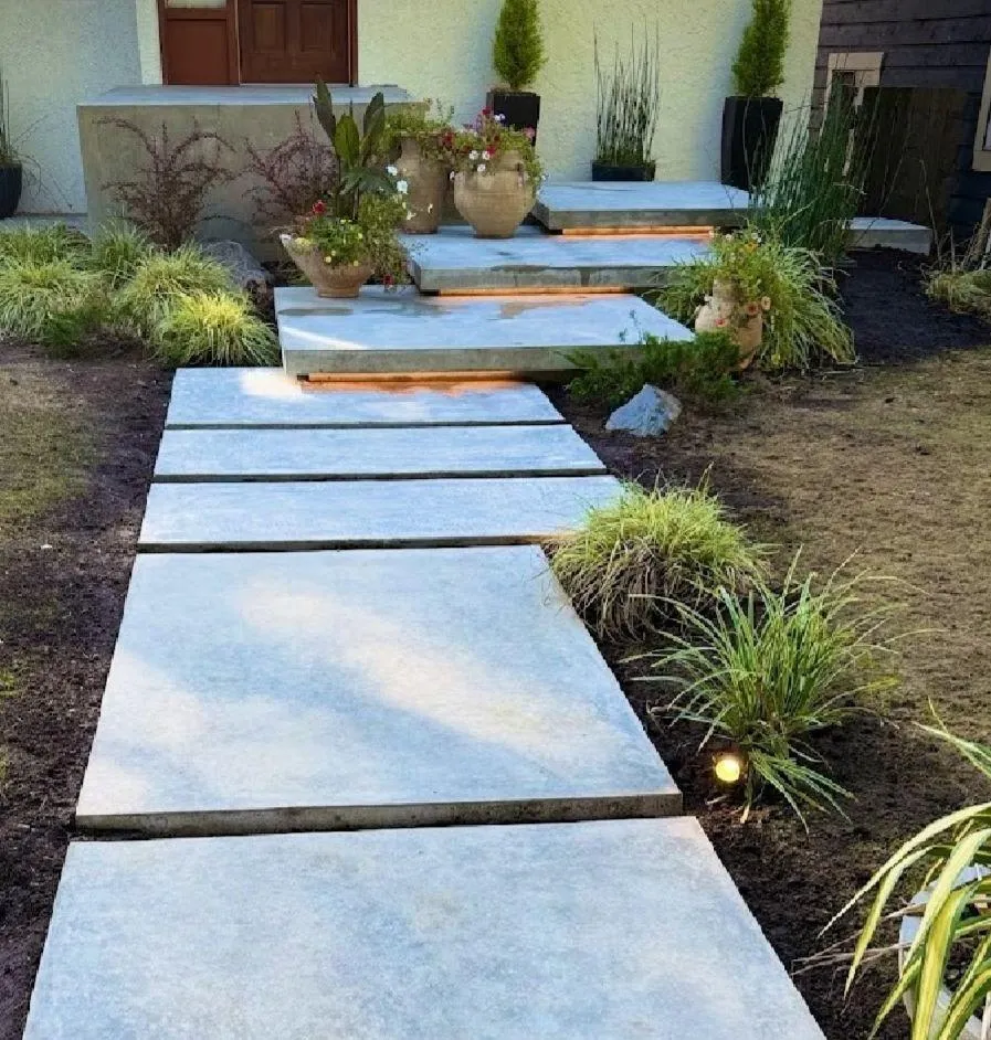 A sunlit pool deck made of textured concrete, surrounding a rectangular pool. The surface is slip-resistant and features a subtle color blend, with lounge chairs and greenery creating a relaxing atmosphere.
