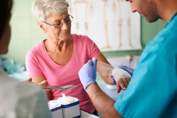Royal Wound Care clinician applying professional wound dressing to elderly patient's hand, promoting safe and effective outpatient wound care services.