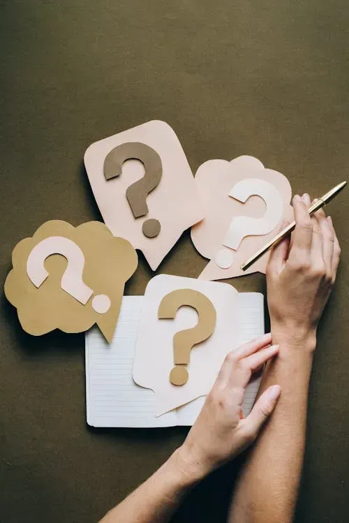 Honor and Clarity Coaching Ministry  - Rebecca & Bill Alderman - Multiple Question Mark Signs, different colors, with one female hand holding a pen over a notebook