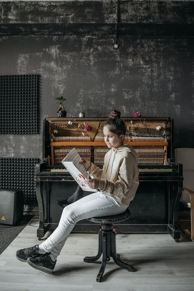 Girl sitting on stool in front of a piano looking over her music.