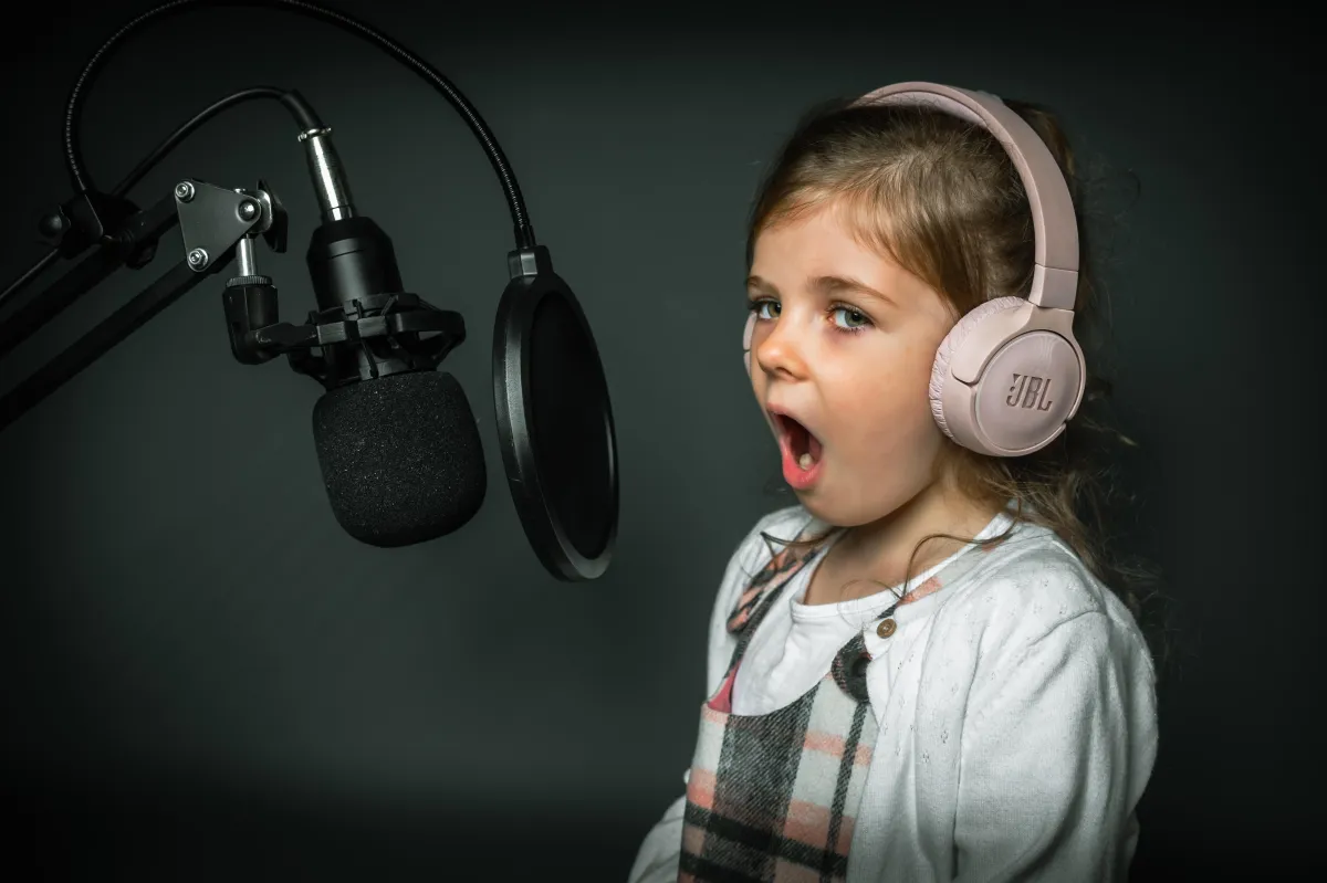 Child wearing headphones, standing in front of a microphone, with wide mouth opened, ready to sing.