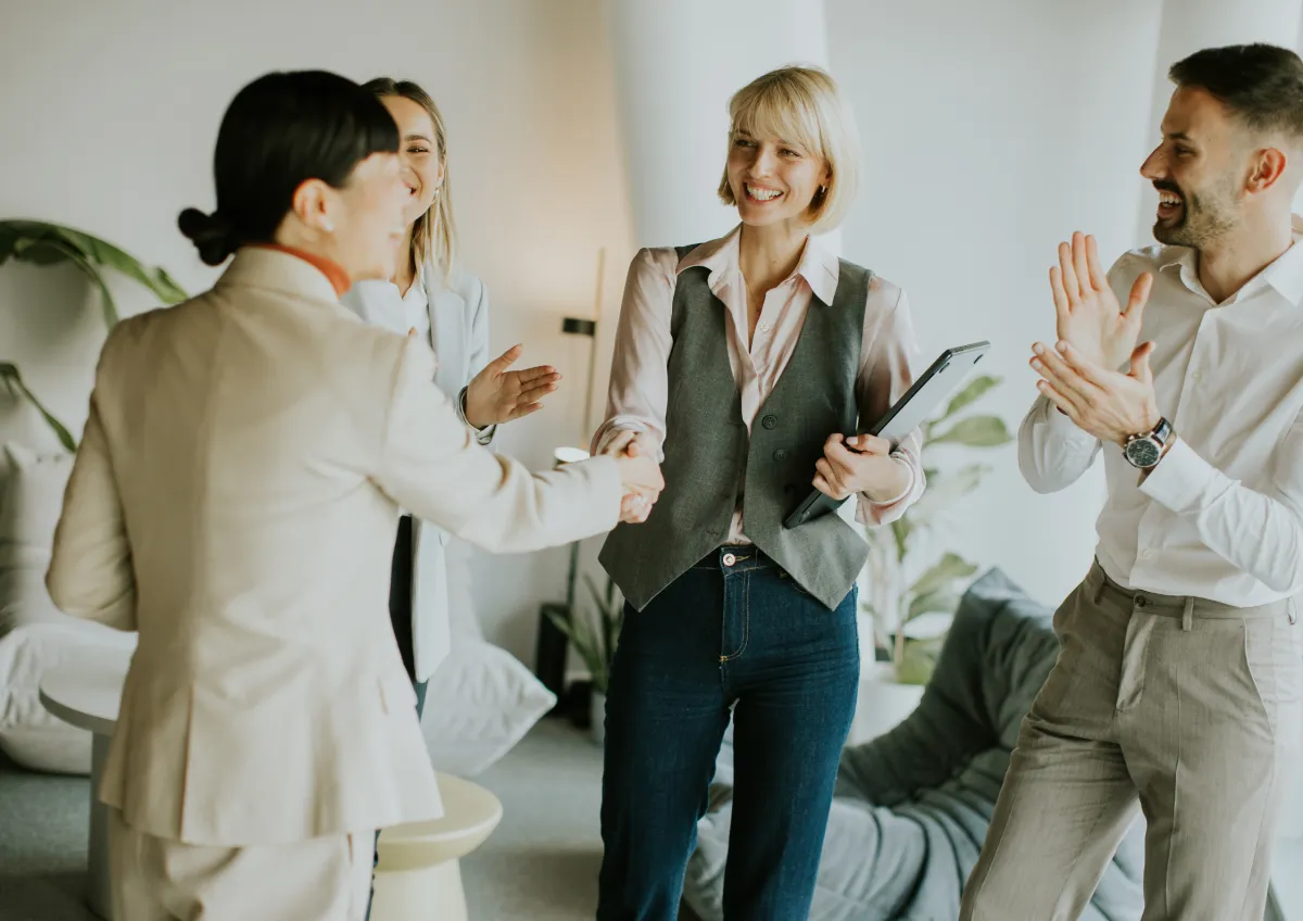 A cheerful real estate agent celebrating a successful referral in a modern office, holding a congratulatory email on a tablet. The background features a vision board with client photos and referral milestones, creating a sense of achievement and motivation.