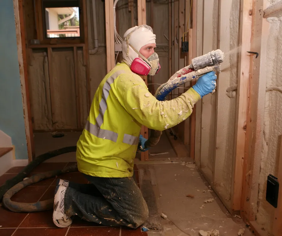 Spray foam insulation being sprayed by man in yellow shirt