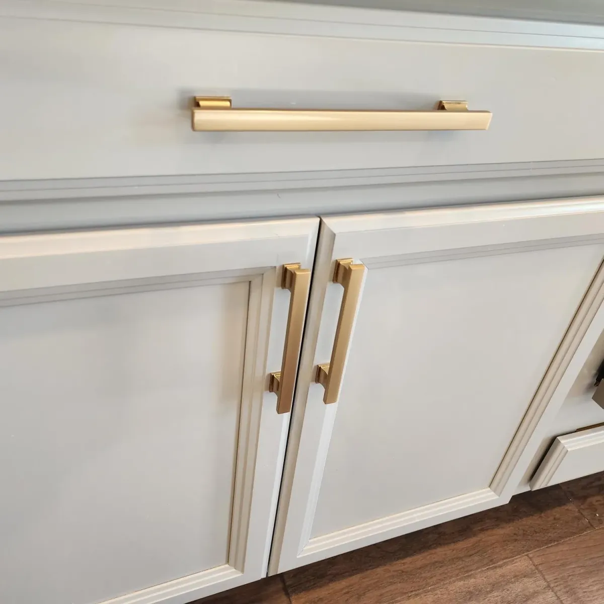 Finished modern cabinet hardware on freshly painted wooden cabinets in a bright upscale kitchen with natural sunlight.
