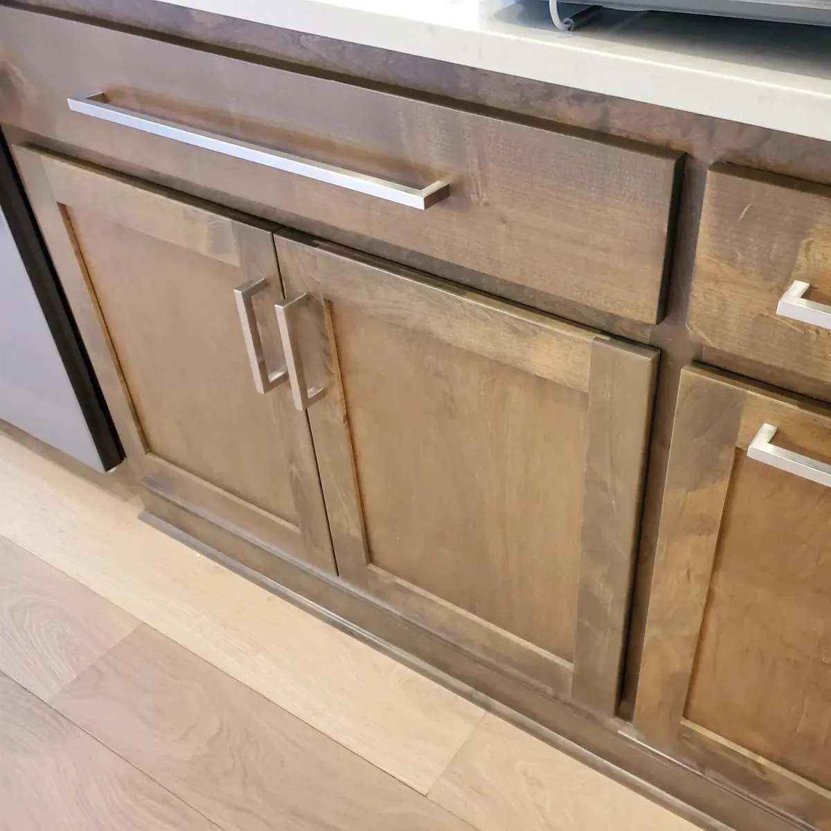 Shiny stainless steel cabinet handles and knobs installed in a modern kitchen with wooden cabinets and granite countertops