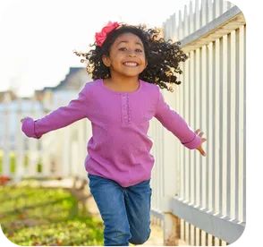 Smiling young girl standing confidently with her hands on her hips, surrounded by a serene park background.