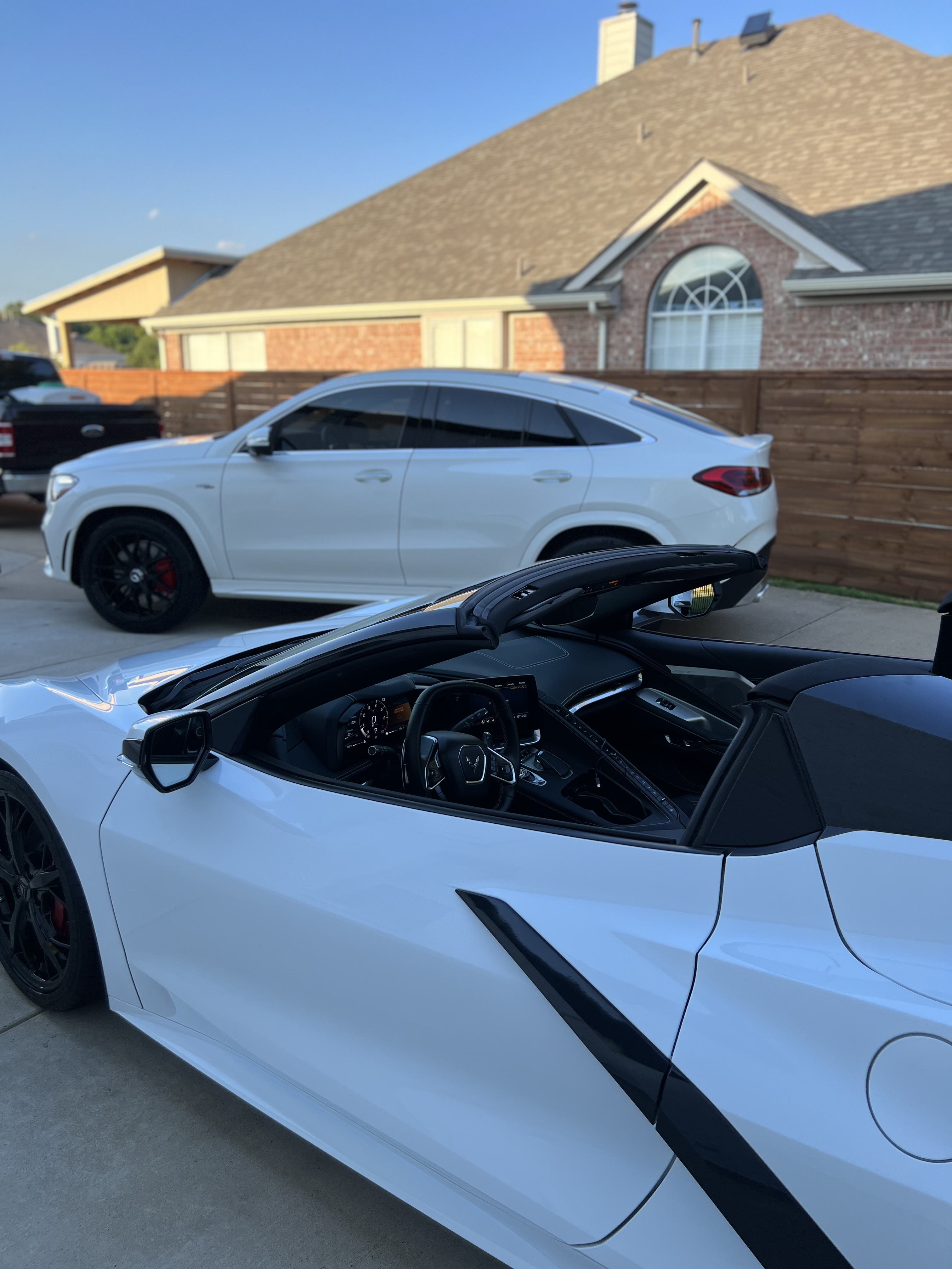 White Corvette with roof down and white Mercedes in the background