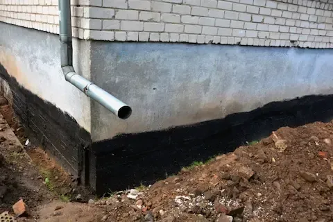 Foundation waterproofing in progress with fresh tar membrane applied to a home's exterior wall