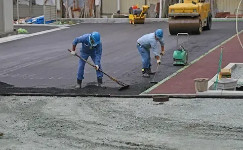 Concrete finishers smoothing a freshly poured asphalt and concrete surface during a paving project