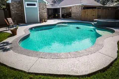 In-ground pool surrounded by a textured concrete deck in a residential backyard