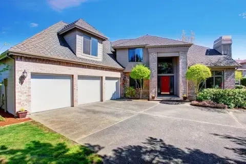 Brick residential home featuring a wide concrete driveway leading to a three-car garage