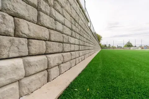 Decorative stacked-block concrete retaining wall bordering a turf athletic field