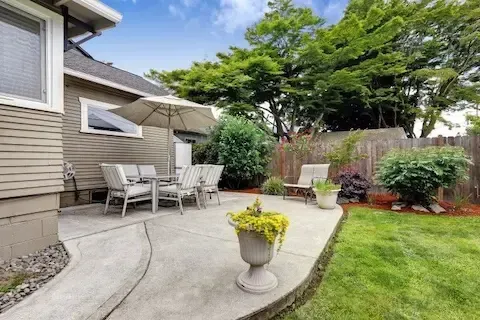 Curved concrete patio in a landscaped backyard with outdoor seating and umbrella