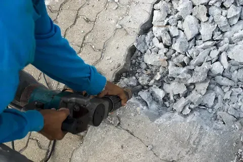 Worker using a jackhammer to break up an old concrete slab during a removal and replacement job