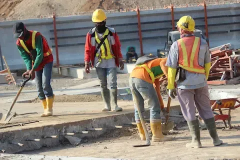 Concrete construction crew in safety vests and hard hats finishing a poured concrete site