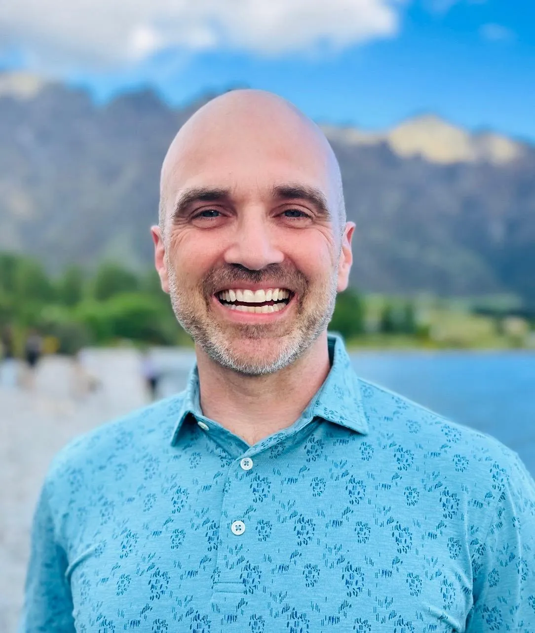 Dr. Danny McGee, board‑certified family medicine physician and founder of Practice Health Hub, smiling outdoors with mountains and lake background.